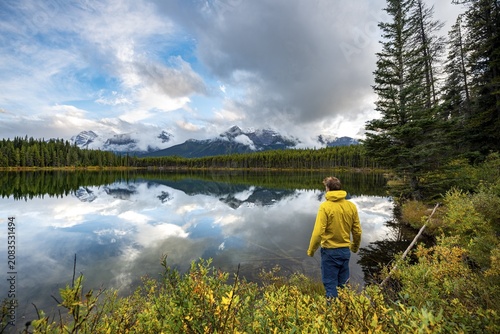 Hiker at the lakeside looking at mountains, autumnal Herbert Lake, mountains of the Bow Range reflected in the lake, Banff National Park, Canadian Rocky Mountains, Alberta, Canada