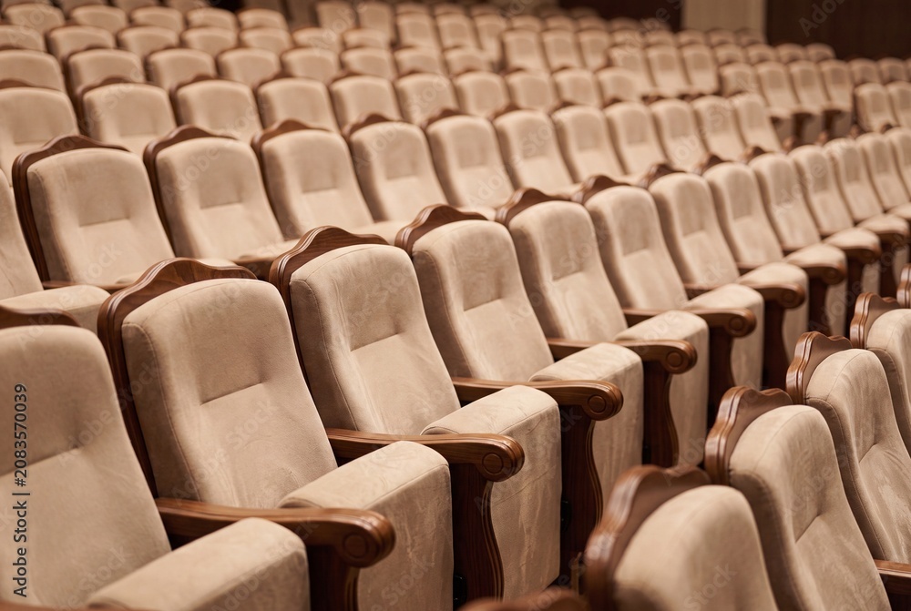 Fototapeta premium Rows of empty beige velvet theater seats in a dimly lit auditorium