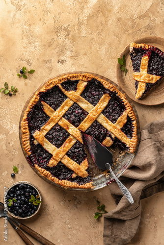 Blueberry pie with lattice crust sliced on brown textured table background, traditional homemade dessert concept top view