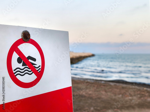 Close up of a no swimming warning sign on a beach with a blurred sea background