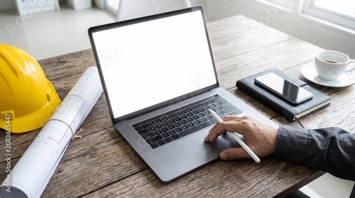 Using a laptop with blank screen on a desk with blueprints and hard hat
