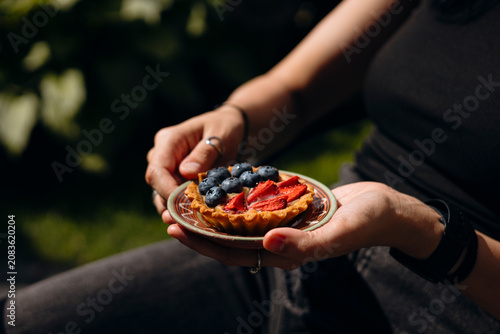 Canvastavla Woman holding fresh berry tartlet outdoors in summer.