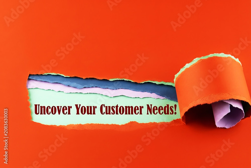 Uncover Your Customer Needs Message Revealed Through Torn Paper On Bright orange Background For Marketing Research And Business Strategy Concept