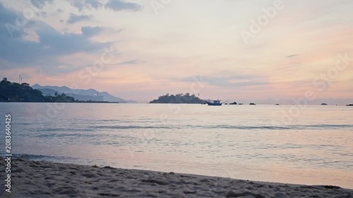 Calm tropical beach at sunrise with distant boat