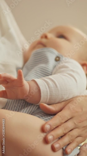 A young mother gently rocks her baby in a softly lit nursery, cradling the infant in her arms. The routine of maternal care and tenderness is present as she calms the child for sleep