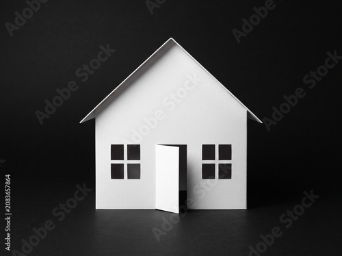 Minimalist white paper house model isolated on pitch black background representing real estate home insurance mortgage and property investment concepts