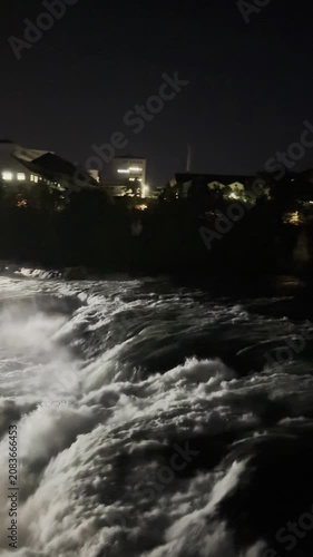 SCHAFFHAUSEN, SWITZERLAND - OCTOBER 11, 2025: Night view of the Rhine Falls area with illuminated riverside, trees and buildings in Schaffhausen, Switzerland.