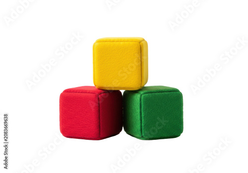 Macro close-up of soft, fuzzy felt toy blocks (red, green, yellow) stacked pyramidically on a reflective white surface against infinity background, concept of early structural learning