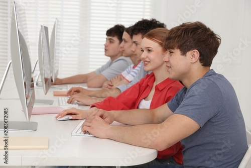 Group of teenagers using computers at white desk in class  selective focus