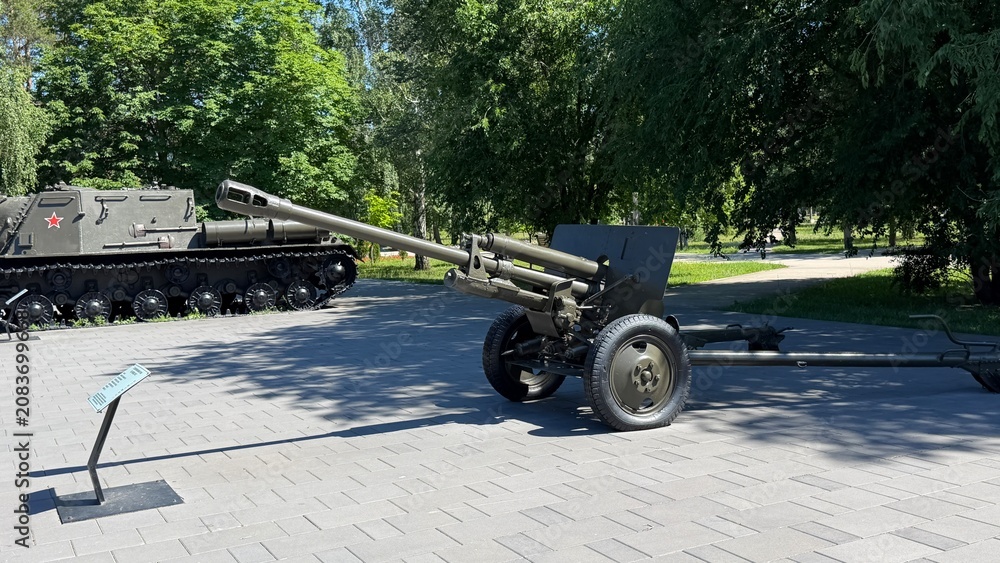 Obraz premium Military Memorial: A historical artillery piece stands as a monument in a park, with a military vehicle visible in the background, evoking remembrance of past conflicts.