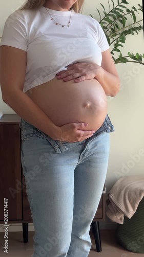 UGC-style vertical phone video of a pregnant woman cradling her bare baby bump at home, an authentic candid symbol of anticipation and motherhood
