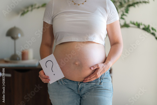 Fotografía Pregnant woman holding a hand-drawn question mark card against her bare belly, s