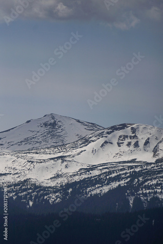 Snow covered mountain peaks close up under a moody grey sky with copy space for text.