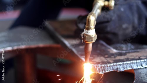 Close-up of an oxy-fuel cutting torch slicing through a thick steel plate with bright sparks and molten metal in a workshop.
