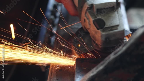 Close-up of a worker operating an electric angle grinder on a steel structure, producing a stream of bright sparks in a workshop