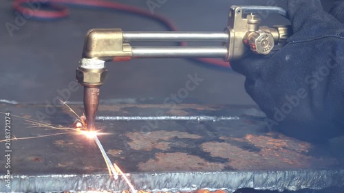 Close-up of an oxy-fuel cutting torch slicing through a thick steel plate with bright sparks and molten metal in a workshop.