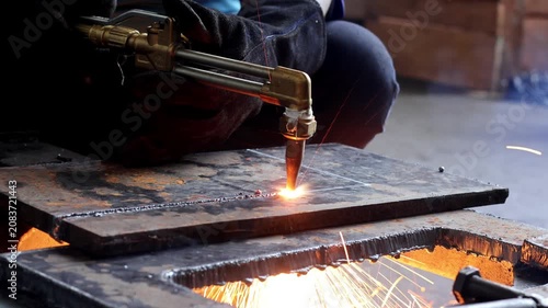 Close-up of an oxy-fuel cutting torch slicing through a thick steel plate with bright sparks and molten metal in a workshop.