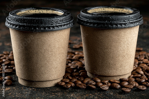 Two disposable paper coffee cups sitting on roasted coffee beans