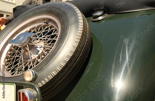 Close-up of a vintage car's spare tire and fender with chrome details. Detailed view of a classic automobile's spoked wheel, rubber tire, and shiny green bodywork, highlighting its retro design