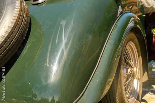 Close-up of a vintage green car's rear fender and spare tire. Detailed view of the curved fender, wire wheel, and external spare tire on a classic automobile, showcasing its aged charm and design