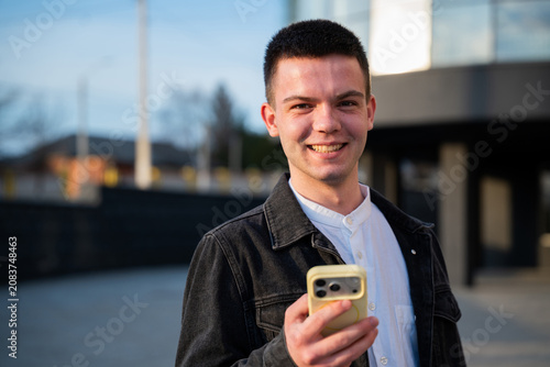 Bild auf Leinwand Smiling young man holding smartphone outdoors near modern office building