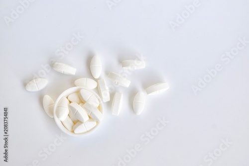 Konstfotografi Direct top view of white oval pharmaceutical caplets scattered organically around a small white plastic container cap on a seamless white studio background
