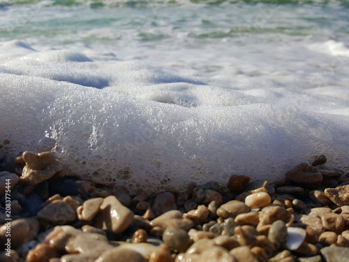 Sea foam washing over pebbles on a rocky beach. Natural coastal texture with ocean waves, shoreline details and refreshing seaside atmosphere.