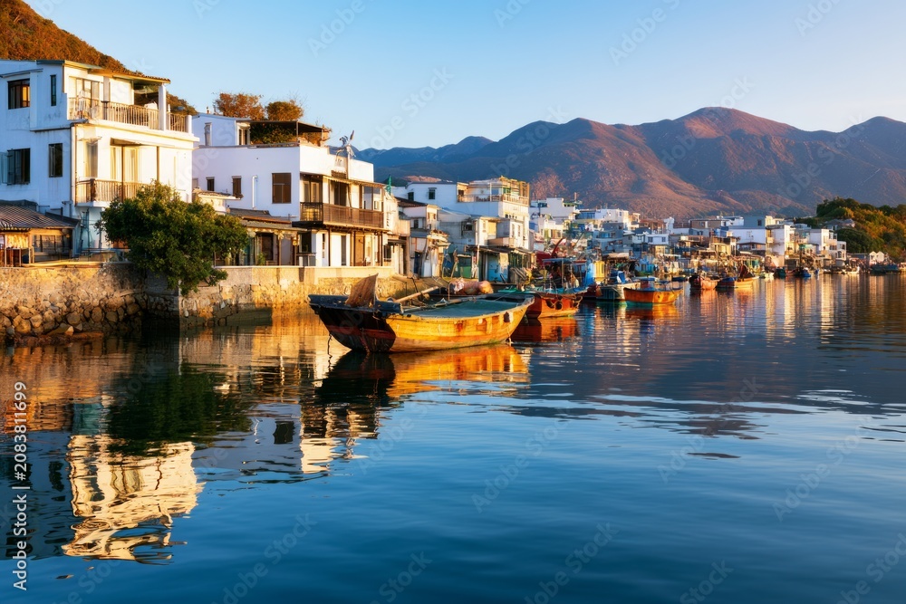 Fototapeta premium Traditional Coastal Settlement with Fishermen's Boats Reflecting in Calm Waters at Sunrise