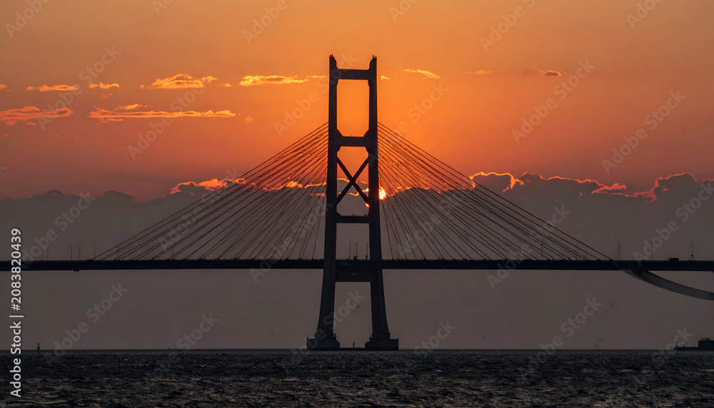 Obraz premium Iconic Suspension Bridge Tower Silhouetted Against Dramatic Sunset Sky.