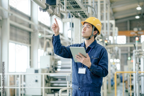 タブレットを使って工場設備を点検するヘルメットを着用した日本人若手男性エンジニア