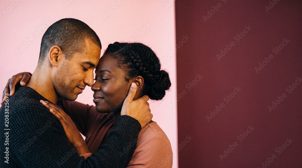 Obraz premium Intimate portrait of a romantic multi-ethnic couple touching foreheads with eyes closed against a dual-tone background