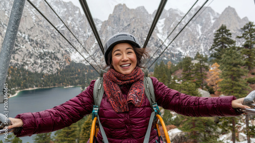 Happy woman wearing helmet and warm jacket enjoying zip line adventure in snowy mountain forest landscape