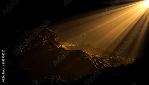 Dramatic golden sunbeams illuminating textured mountain peaks at dawn, atmospheric light rays creating depth and shadow, spiritual or mystical landscape