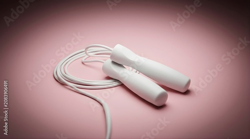 White jump rope with plastic handles coiled on a soft pink surface for fitness training and aerobic exercise routines