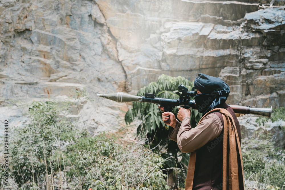 Fototapeta premium Outdoor military concept. Armed man aiming rocket launcher outdoors, tense combat pose with rocky cliff backdrop