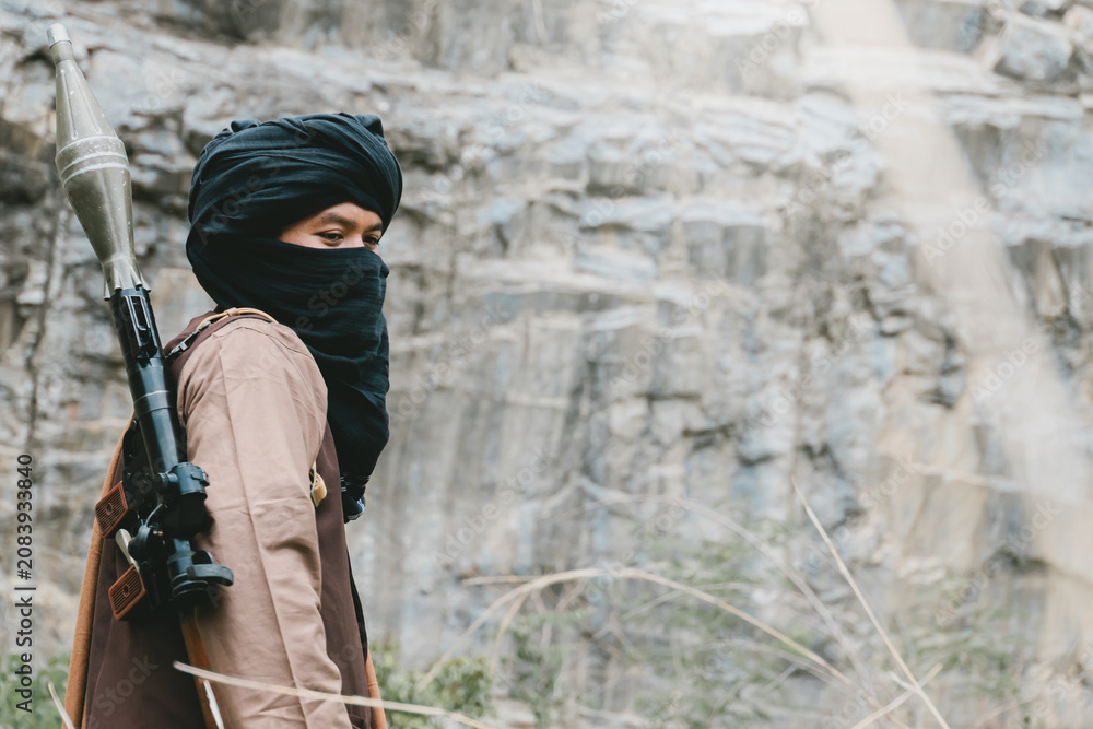 Fototapeta premium Outdoor military concept. Masked person with rocket launcher near rocky cliff in outdoor wilderness setting