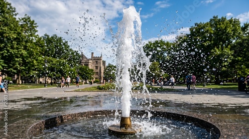 Refreshing water fountain jet spraying upwards in a lush green city park with old architecture