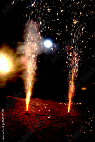 Ground Firework Fountains – Twin Orange Yellow Sparks with Smoke and Glowing Particles on Cobblestone Surface Against Dark Festive Night Concept