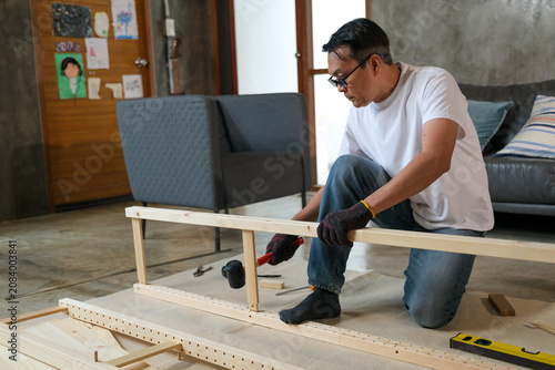 senior Man furniture assembly wood plank home room tool glove kneeling, focused adult building wooden frame on floor during home improvement project
