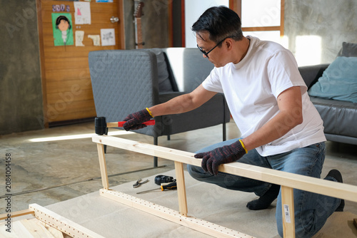 senior Man furniture assembly wood frame home glove tool, focused adult builds wooden table base on floor in modern living room with sofa nearby