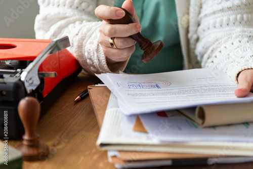 Person stamping documents at a desk with a typewriter and papers.