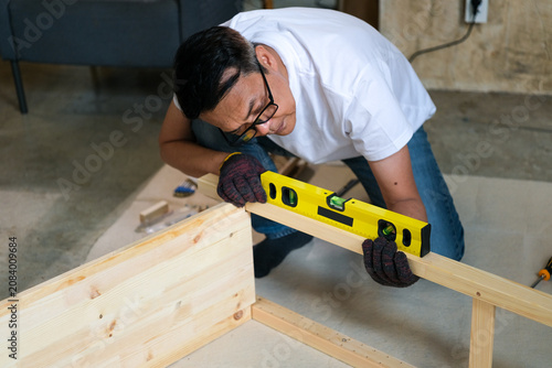 Carpenter wood level workshop construction measurement glove plank focused man checking wooden frame during indoor furniture assembly