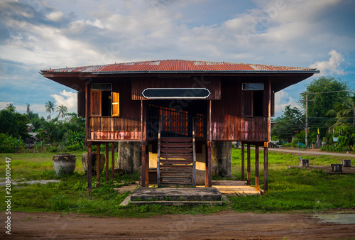 Abandoned Traditional Thai Wooden House on Stilts in Rural Thailand. An old traditional stilt wooden house  in rural Thailand with a corrugated zinc roof, vintage architecture and large water jars.