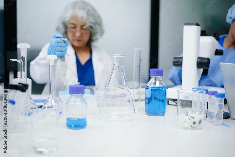 Fototapeta premium Dedicated senior Asian female scientist and her diverse laboratory team conduct advanced medical biotechnology research