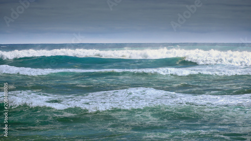 Stormy ocean waves crashing across turquoise sea under overcast sky, rough surf