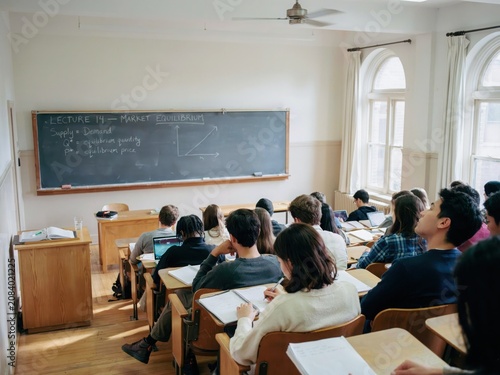 Students sitting in university lecture hall listening to economics professor during market equilibrium class session.