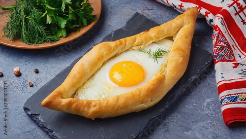 Delicious Adjarian Khachapuri with egg yolk and herbs on a dark stone board.