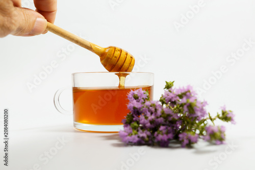 Person adding natural honey to a cup of hot herbal tea using a wooden dipper, promoting health and wellness
