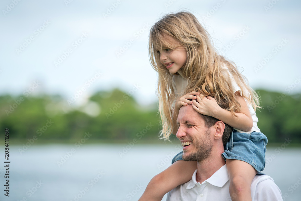 Fototapeta premium Shoulder ride with father and daughter bonding happiness family moment outdoor. Smiling father carrying daughter on shoulders walking in Park Fun Time and Active Parent Child