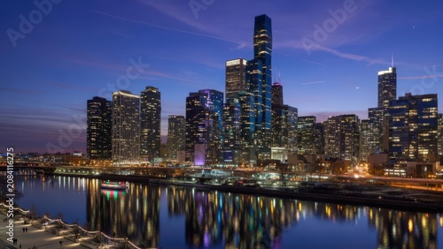 Stunning dusk view of the illuminated chicago skyline showcasing high rise skyscraper towers reflecting brightly over the flowing river during a peaceful evening period in an iconic american city